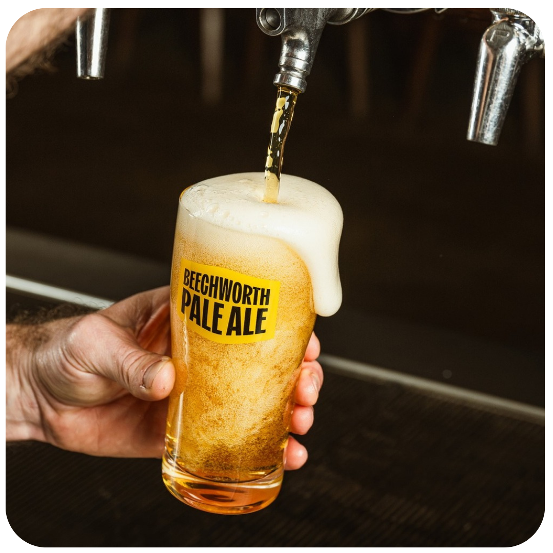 Hand pouring Beechworth Pale Ale into a glass with a dark background