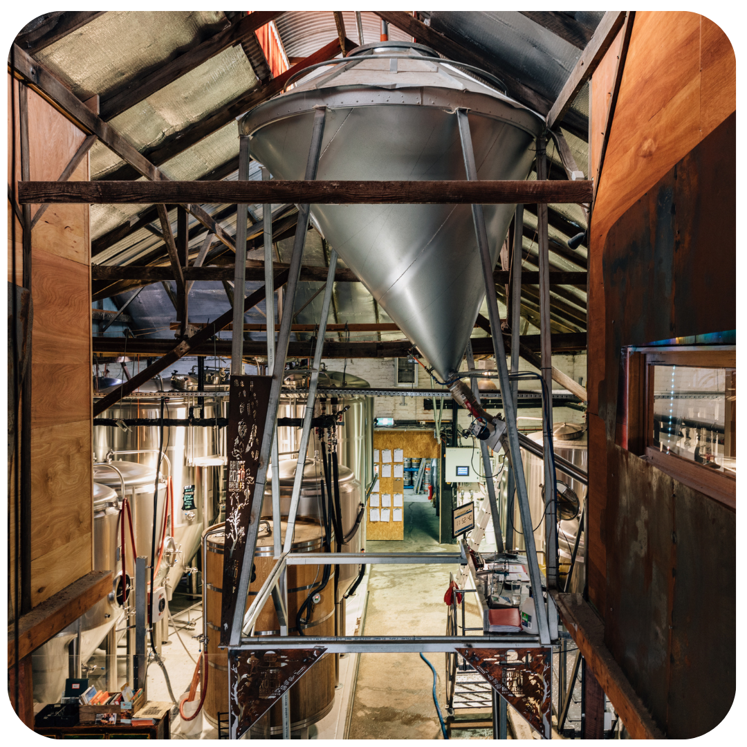 Metal storage tank inside a warehouse with wooden beams and equipment.