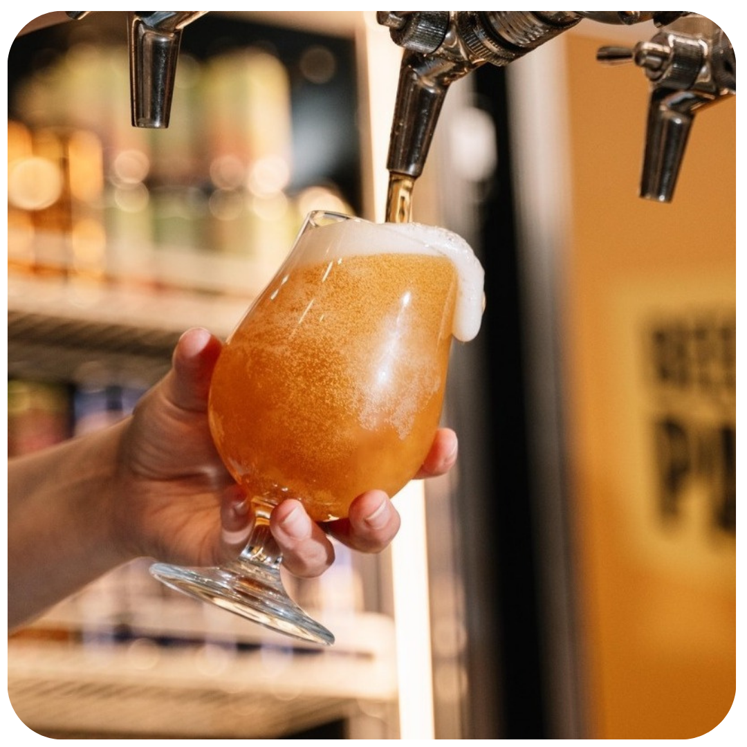 Person holding a glass of beer being poured from a tap.