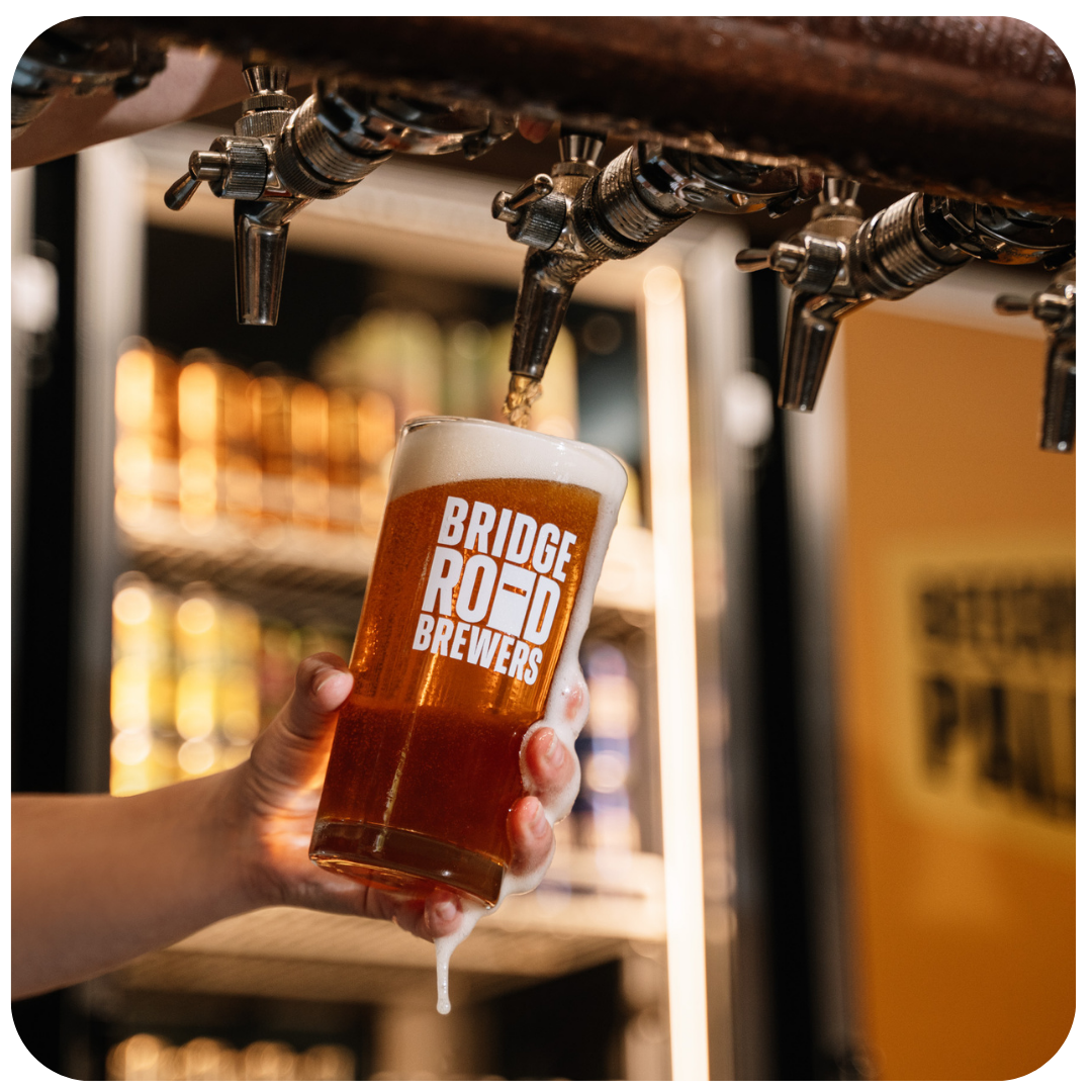 Person holding a glass of Bridge Road Brewers beer being poured from a tap.