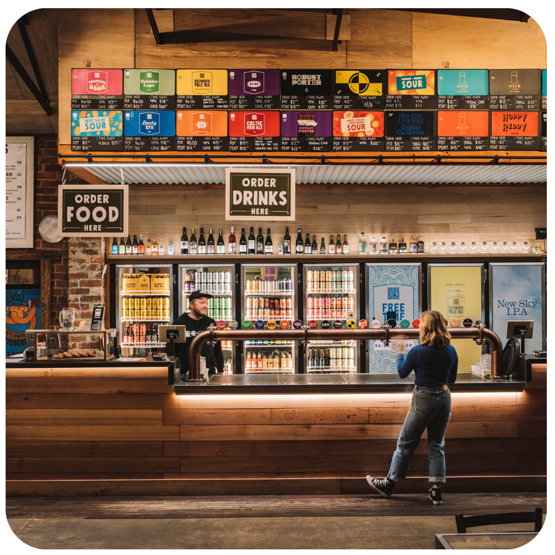Bar with a large drink menu above the counter and a person ordering drinks.